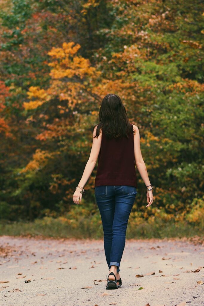 Woman in Brown Sleeveless Dress and Blue Jeans Standing on Gray Path Road